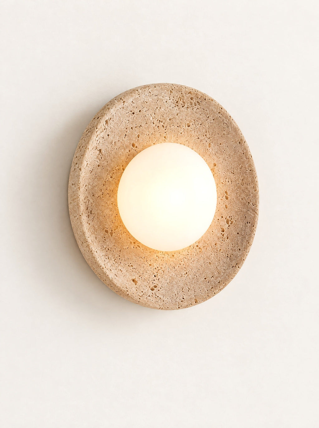 Eclipse Travertine & Opal Sconce switched on, studio photo on a warm white background