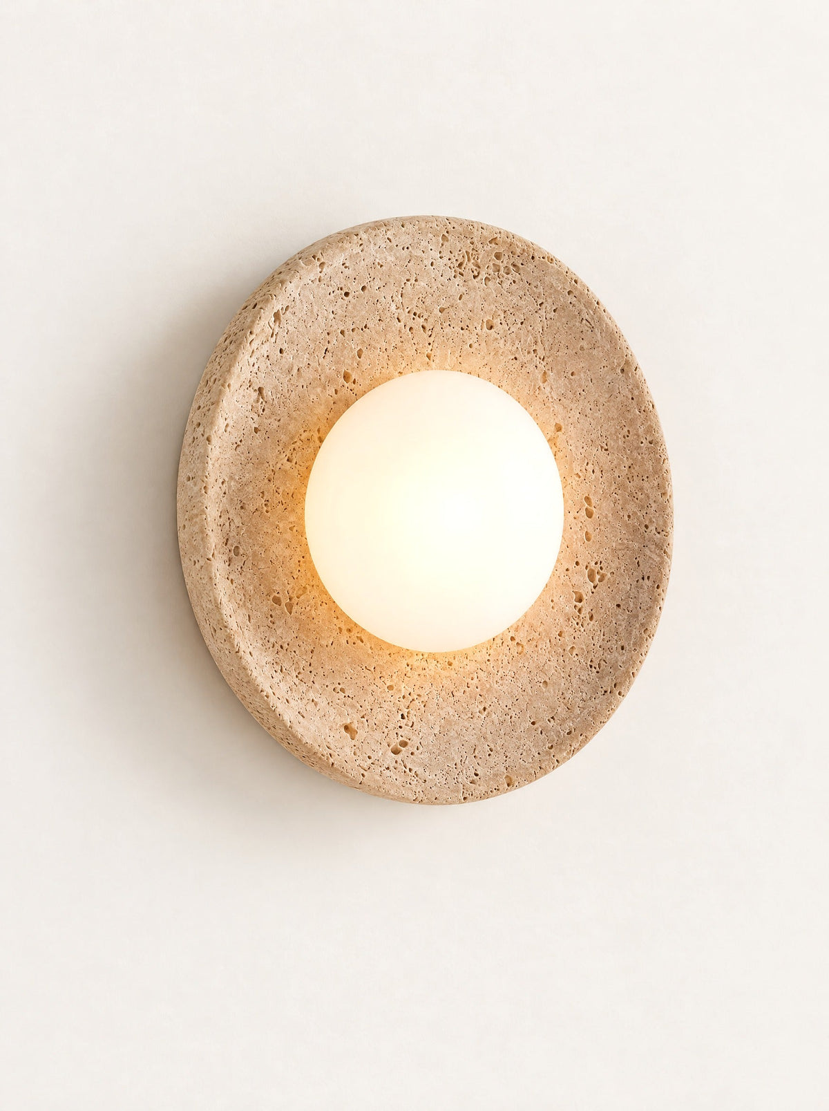 Eclipse Travertine & Opal Sconce switched on, studio photo on a warm white background