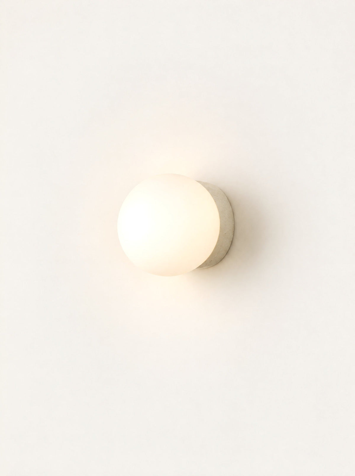 Pebble Glass & Stone Sconce switched on, studio photo on a warm white background