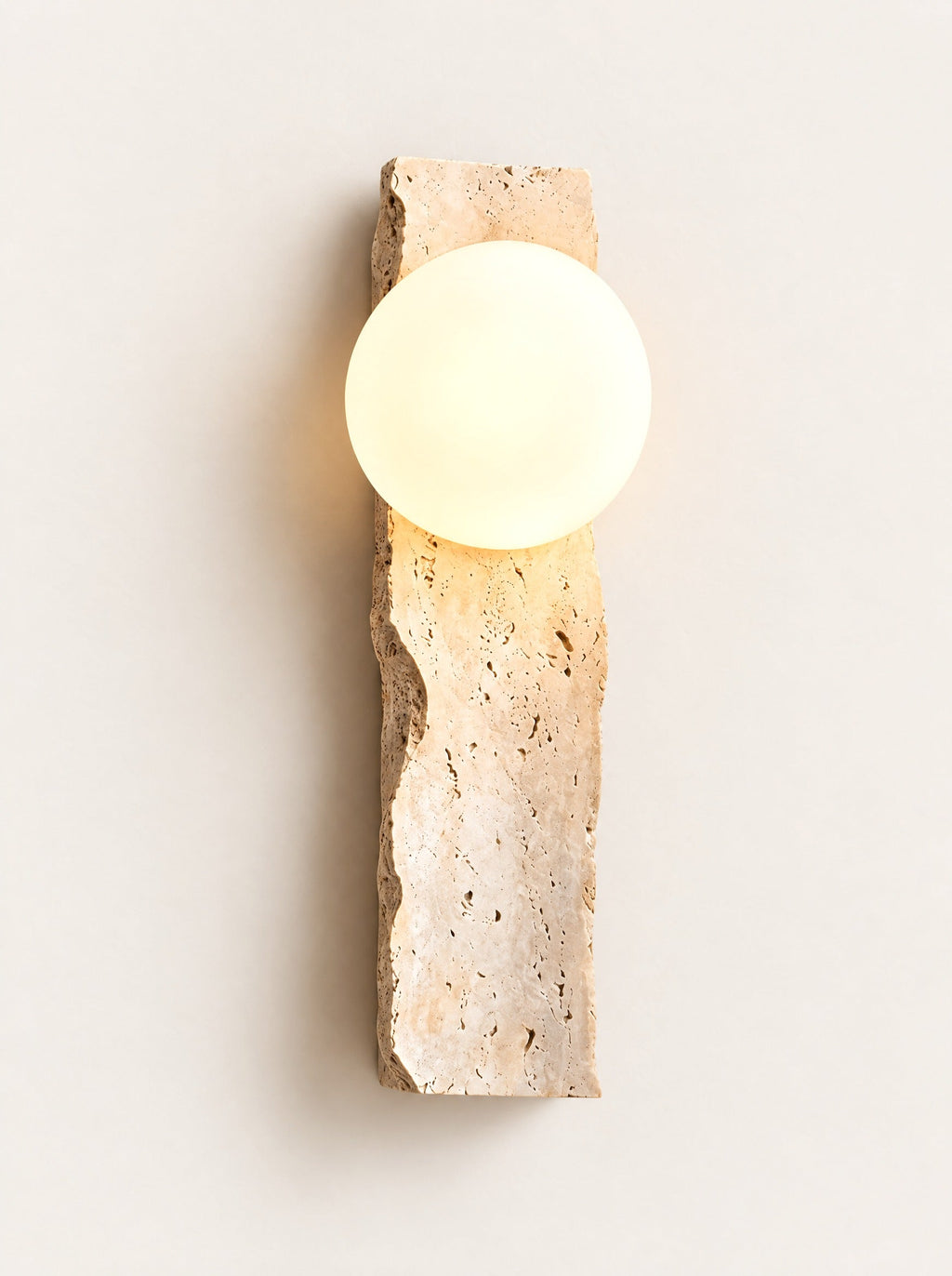 Quarry Travertine Globe Sconce switched on, studio photo on a warm white background