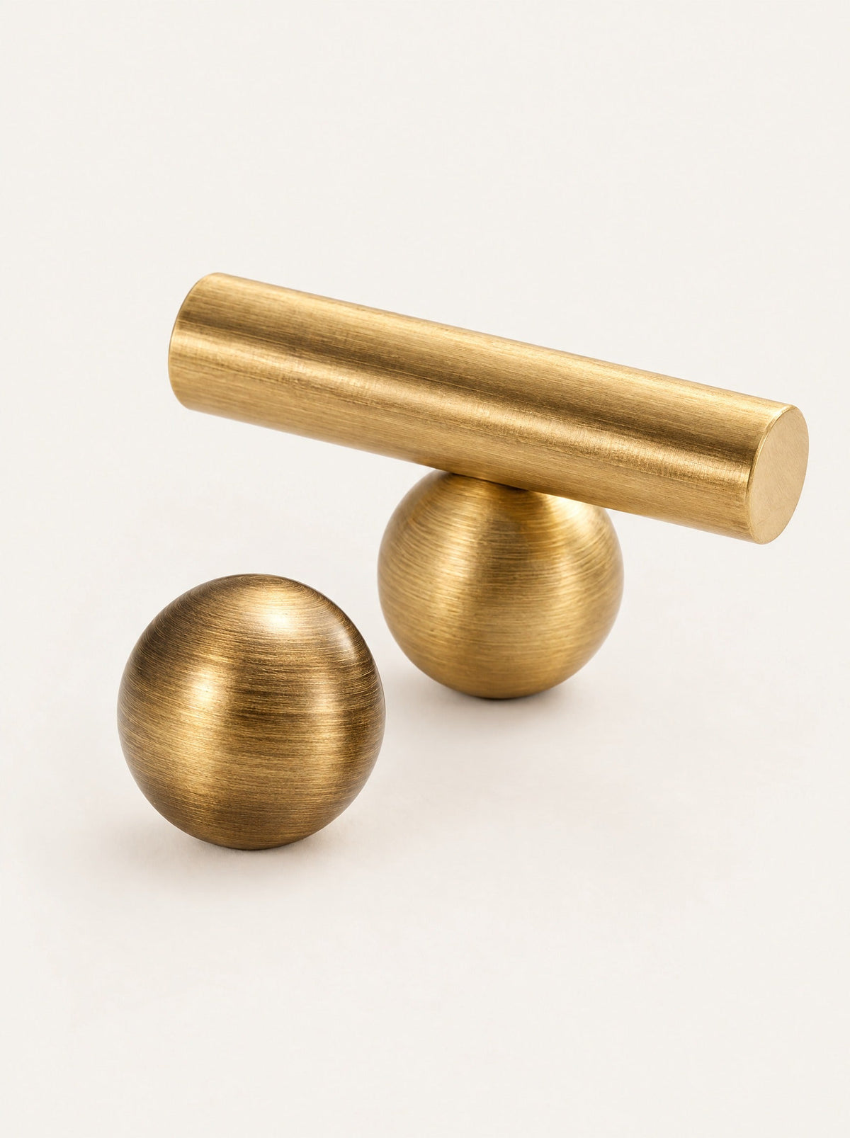 Sphere Brass Knob & Bar Pull, close-up studio photo on a warm white background